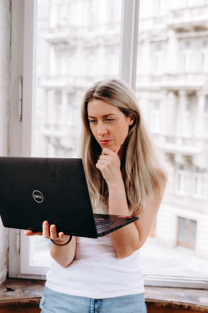 Katka Volková stojí v místnosti s notebookem a přemýšlí